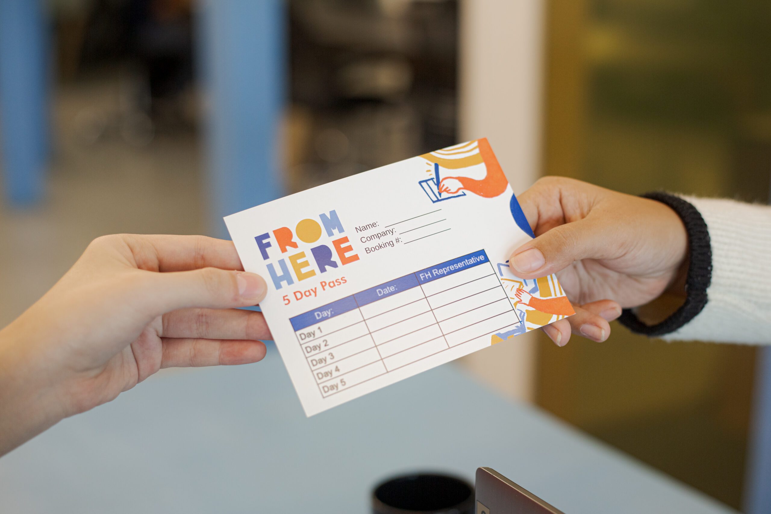 At a modern co-working space reception, a representative is exchanging a branded, colorful pass with a client for access to the shared workspace.
